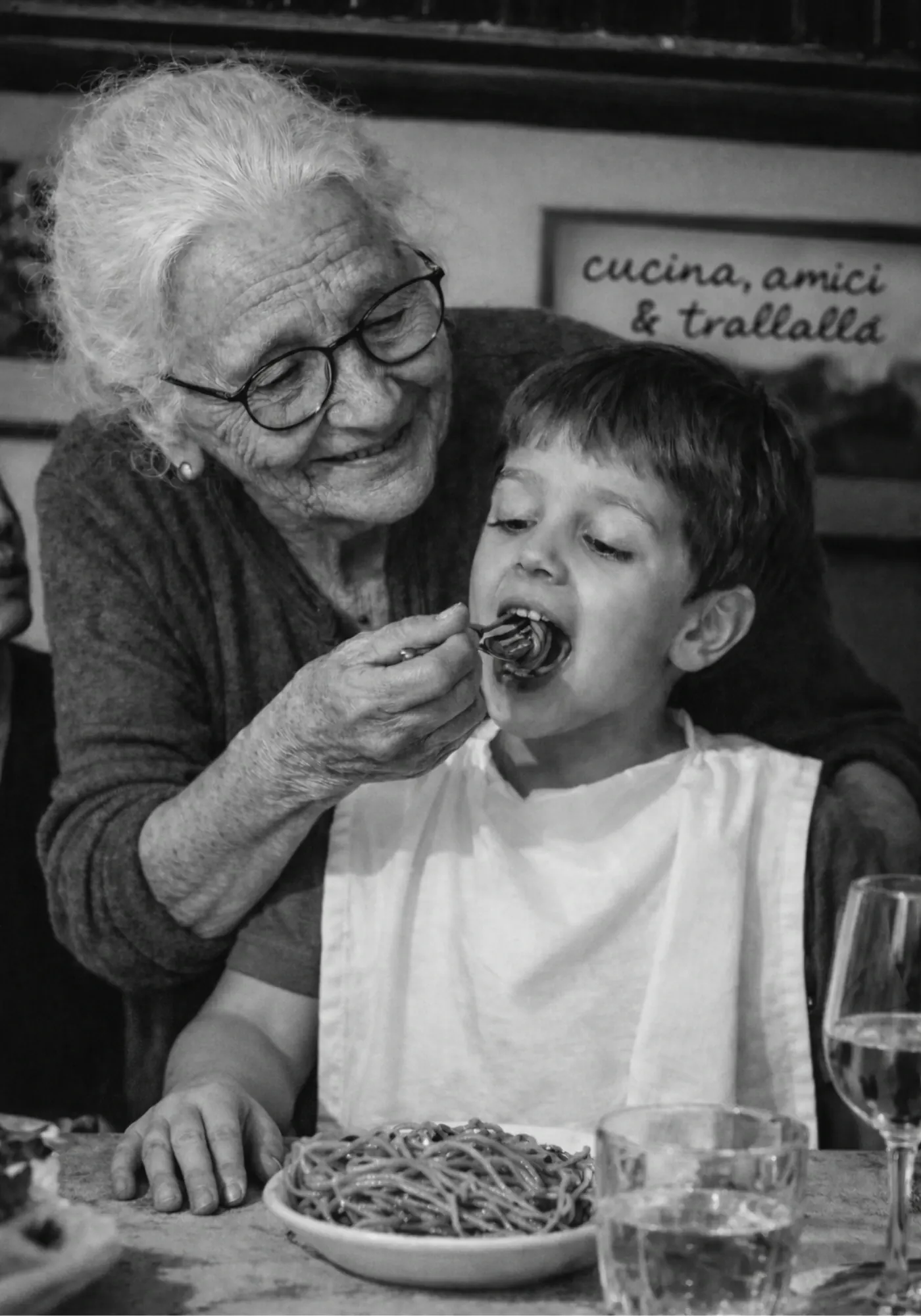 Nonna Peppìna imbocca un bambino a tavola sotto la scritta «Cucina, amici & trallallà»